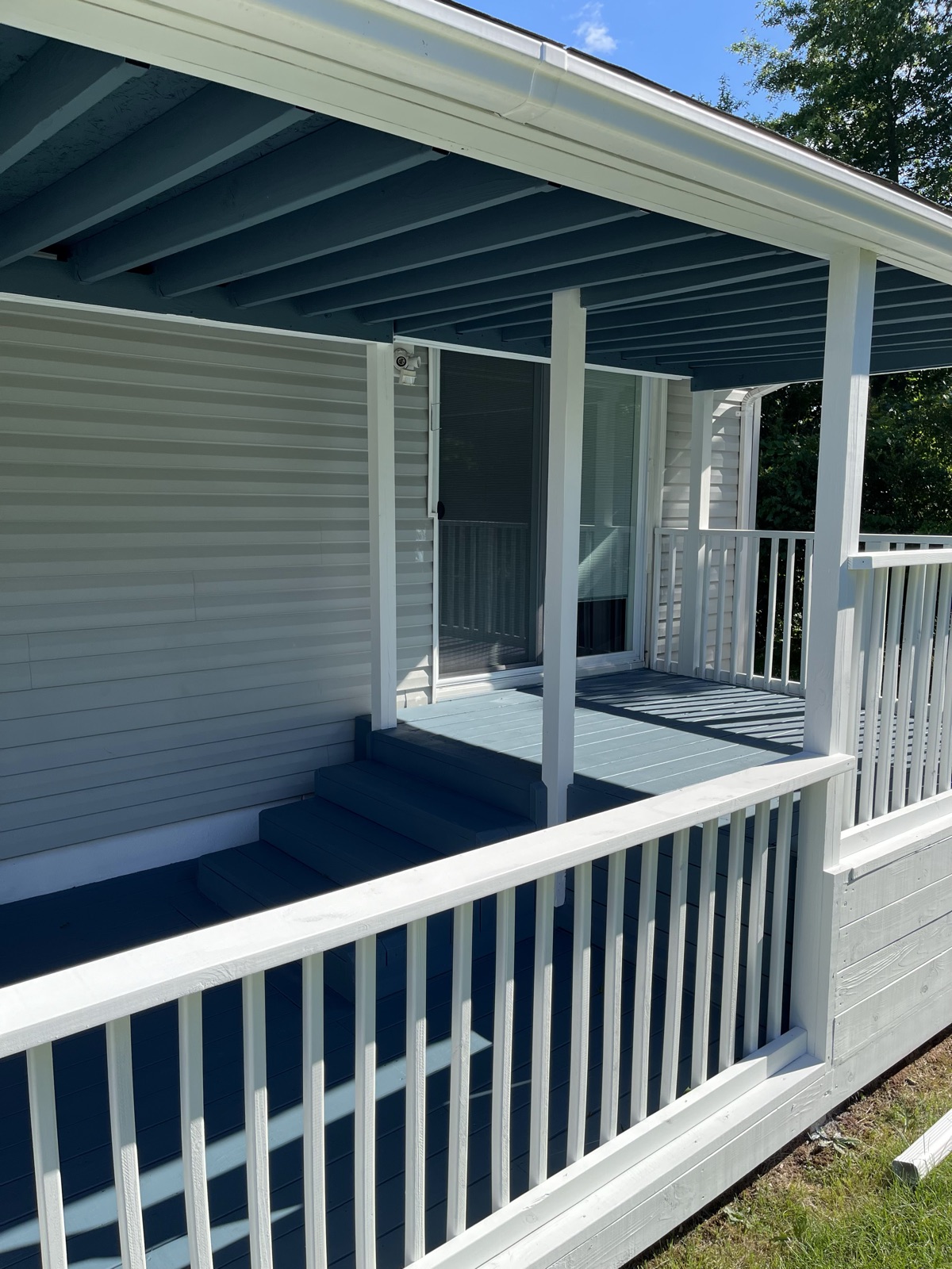 Blue painted covered porch with white railings by J&B Painting